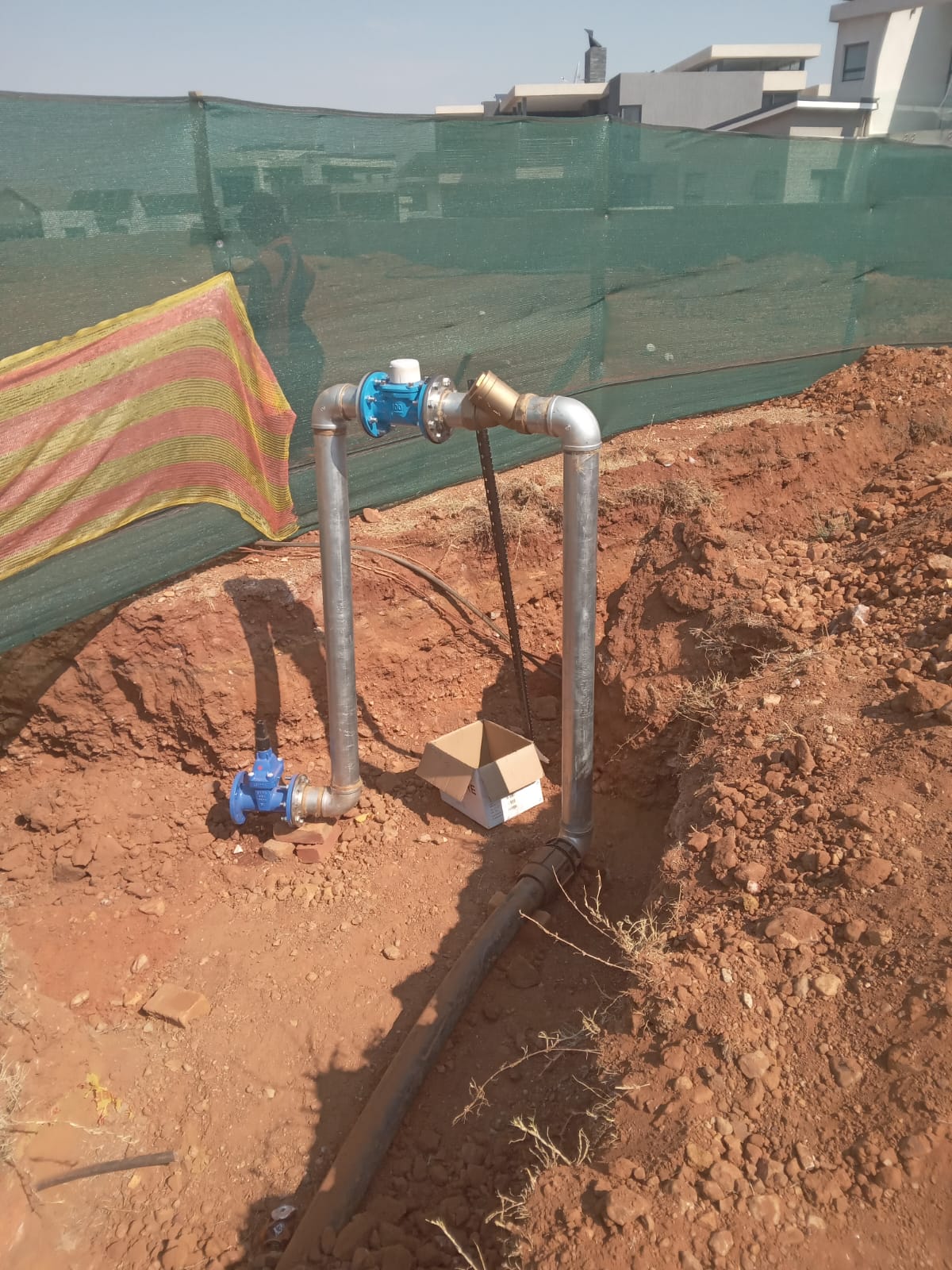 Galvanised borehole riser with blue meter and brass Y-strainer in a trench