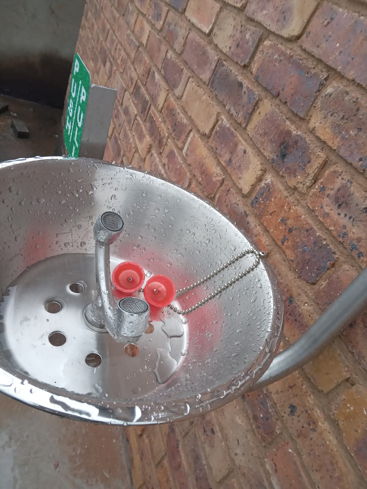 Stainless steel emergency eyewash basin mounted on a brick wall